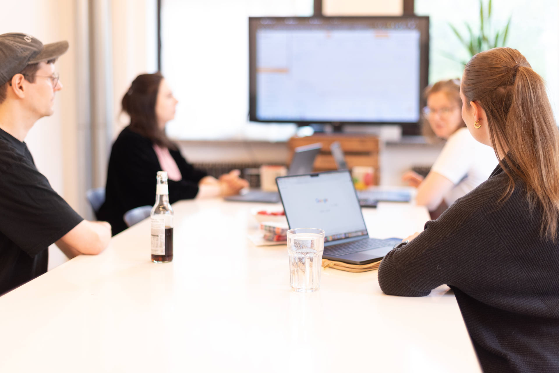 Vier Personen bei einer Besprechung an einem Konferenztisch mit Laptop und Bildschirm